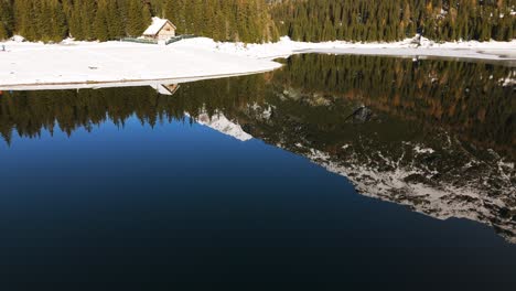 Palù-Italian-alpine-lake-with-hut-and-coniferous-forest-in-winter-season,-Valmalenco-of-Valtellina,-aerial-drone-view