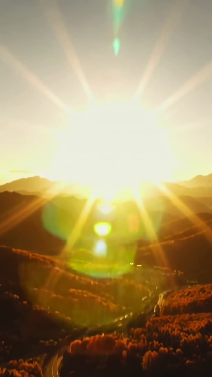 Vertical video: Brightening sun casting lensflare column over mountain valley, showing winding road
