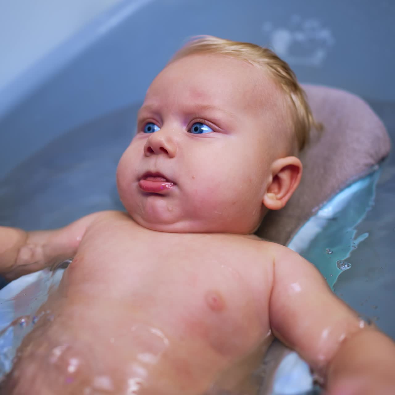 Bebê caucasiano fofo, de cabelo loiro e grandes olhos azuis, deitado em uma banheira. Close-up de um lindo bebê tomando banho