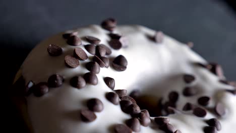 close-up half-shot of delicious glazed white donut with chocolate chips spinning slowly on gray table background.