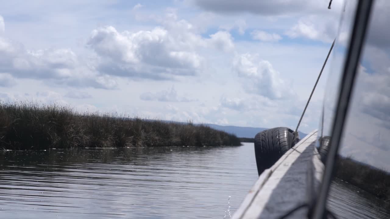 우로스 떠다니는 섬, 페루 - 흐린 화창한 날에 갈대로 덮인 섬을 향해 티티카카 호수를 가로질러 이동하는 관광 보트 - 슬로우 모션