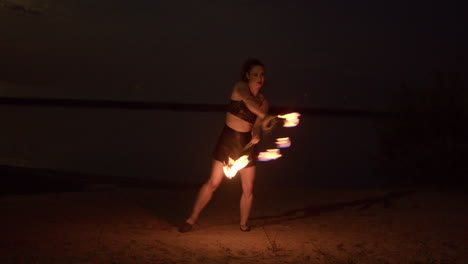 Woman-Fire-Fan-Dancing-on-Lakeside-Beach,-Night-Exterior-Wide-Shot-Slowmo