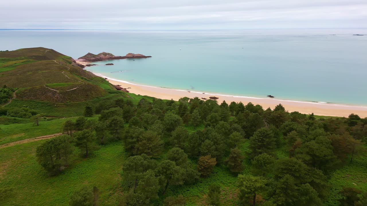 Peaceful location of Cap d'Erquy sandy beach curving below a tree-covered terrain, Côtes-d'Armor, Brittany, France.
