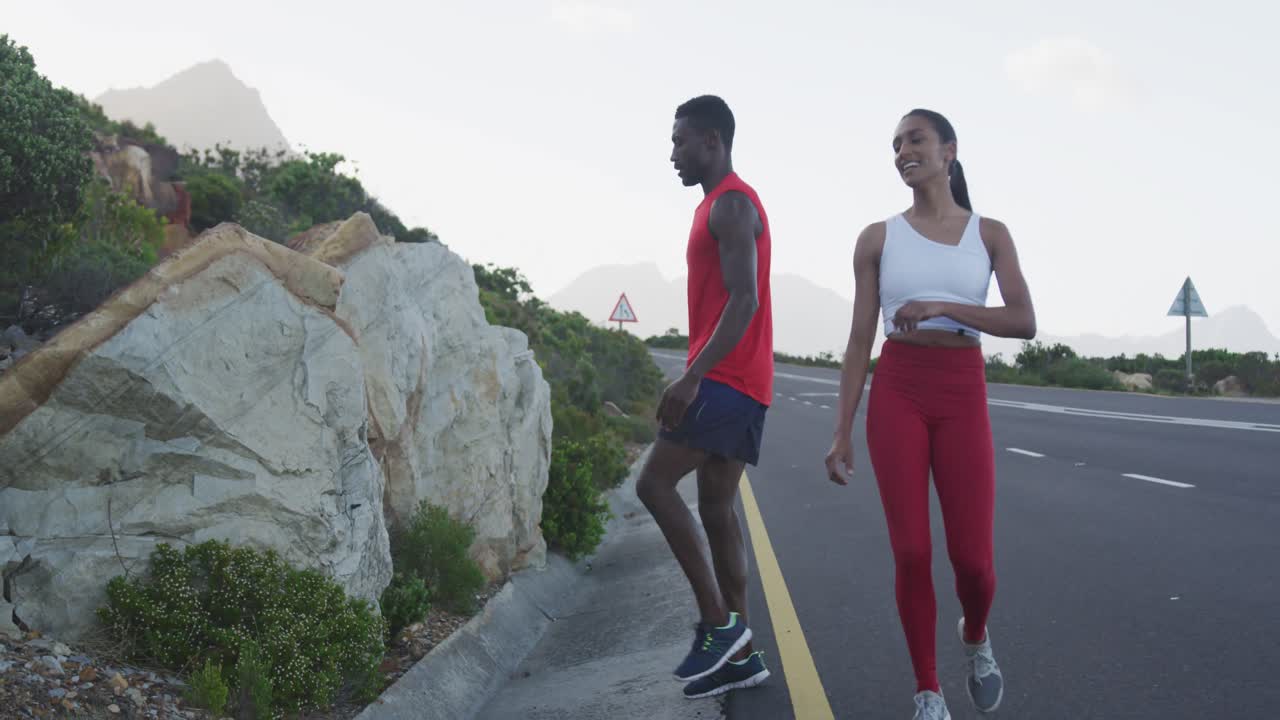 Diverse couple exercising stretching and running on a mountainside country road