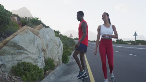 diverse couple exercising stretching and running on a mountainside country road