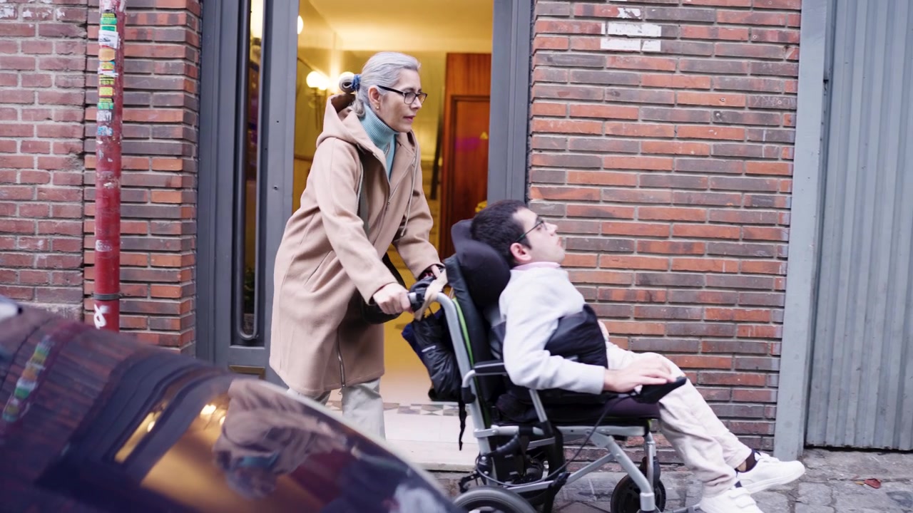 Donna anziana che spinge un giovane uomo in sedia a rotelle fuori da un edificio