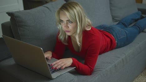 Serious-woman-with-laptop-lying-on-couch