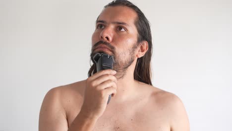 un hombre está usando una afeitadora eléctrica para recortar el bigote y la barba mientras está de pie frente al espejo en el baño en casa