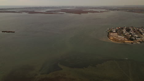 a top-down aerial view over a salt marsh, it is low tide - you can see a sandbar in the waters below. the camera rotates counterclockwise and tilts up to reveal the horizon and the cloudy sky.