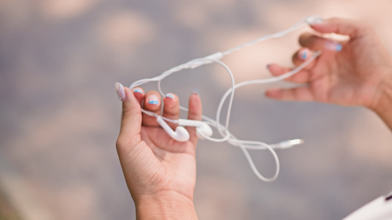 Hands untangle earbuds, Adult hands carefully free tangled wires, Precise movements of hands untangling earbuds calmly, Focused adult hands gently straighten out twisted white earphones