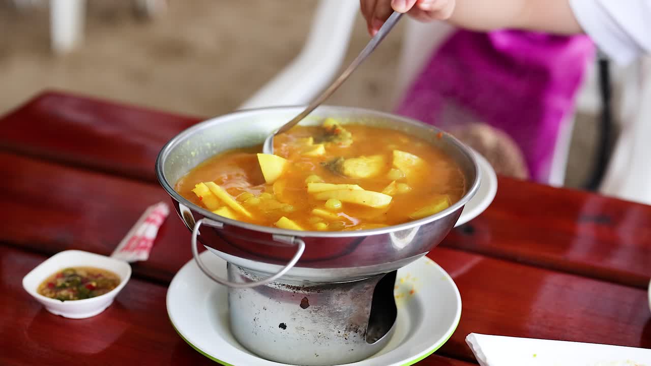 Person serving yellow curry with fish