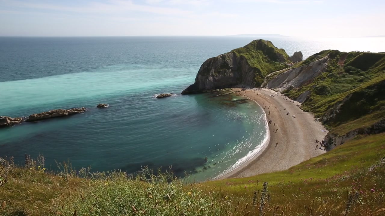 L'arco roccioso di Durdle Door si erge accanto all'acqua turchese a Man o' War Cove, mentre i visitatori si rilassano sulla spiaggia di ciottoli nel Dorset, Inghilterra