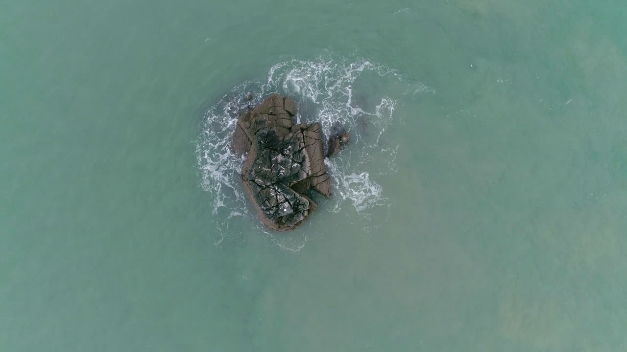 сверху вниз, поднимаясь высоко над одиноким круглым скальным выступом, о который бьются волны открытого океана