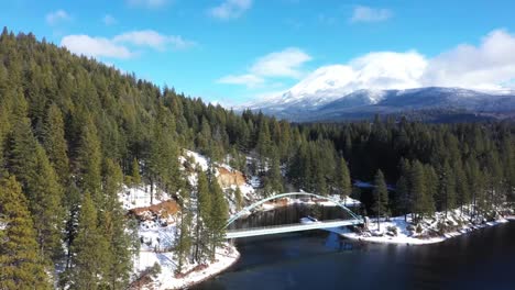 Walking-bridge-across-a-lake-with-light-snow-and-trees-and-Mount-Shasta-in-the-background