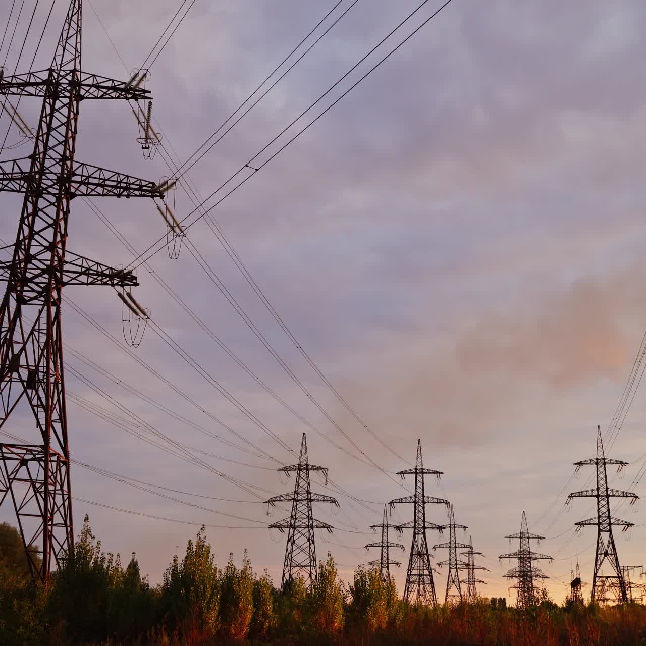 High-voltage electric towers at sunset. Transmission lines on field on the evening sky background. Electricity distribution. View from below.