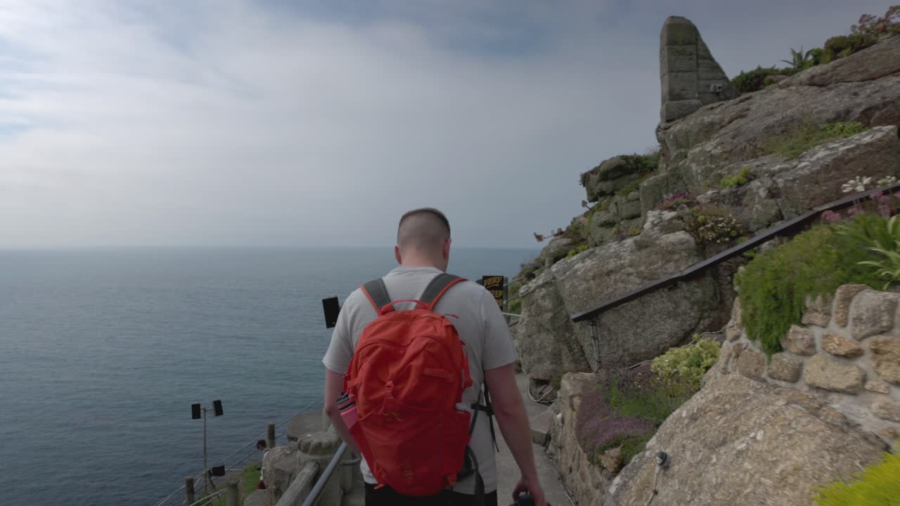 A man walks down a coastal path overlooking the ocean.