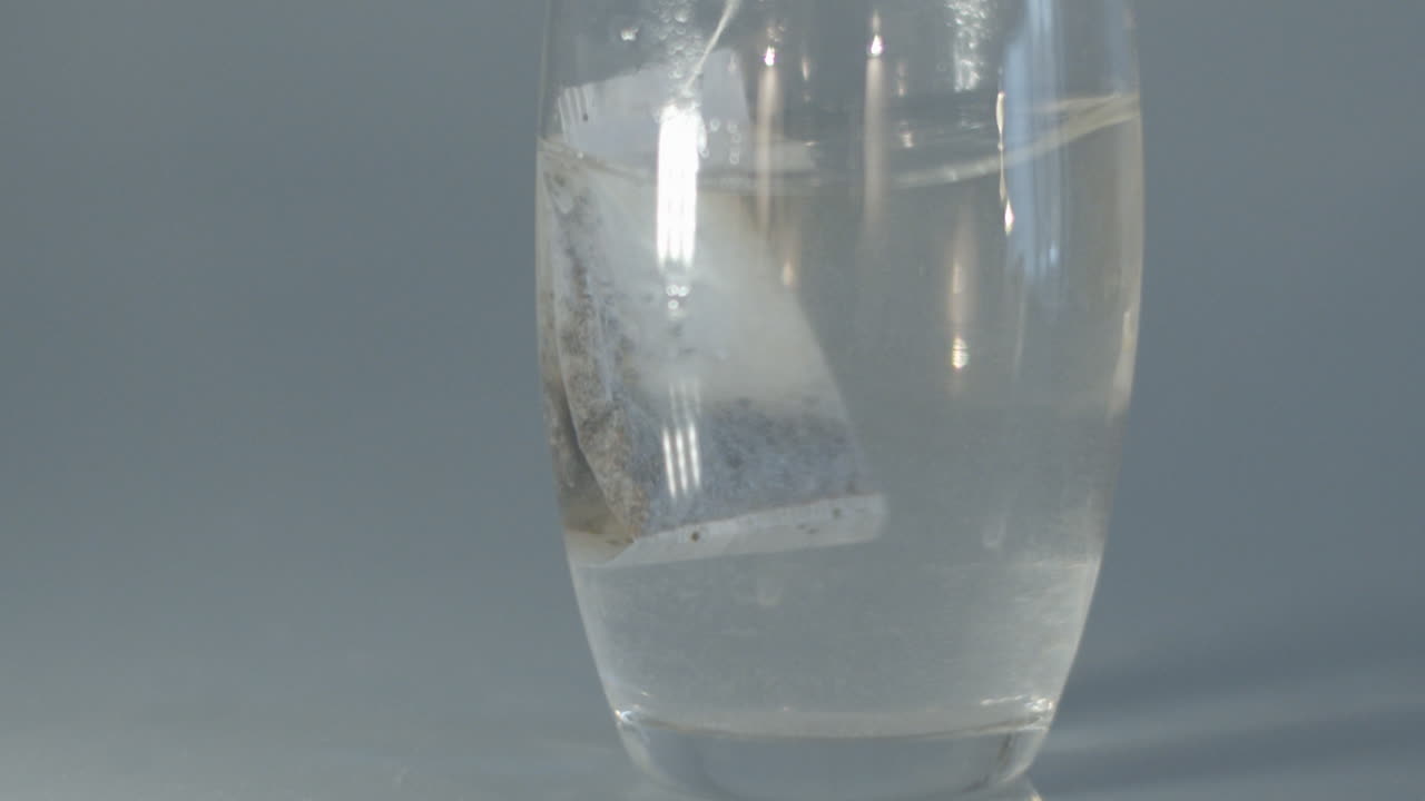 느린 동작으로 뜨거운 물이 담긴 유리잔에서 티백을 옮기고 있습니다.