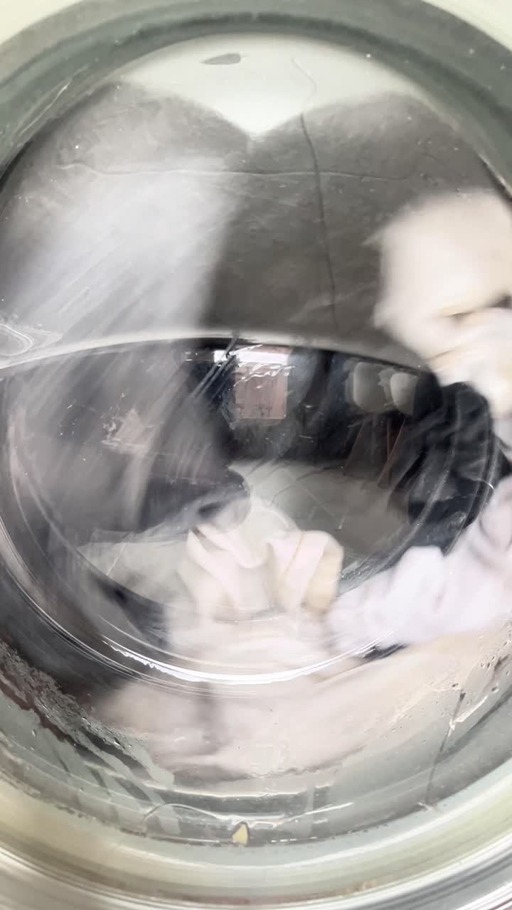 Een wasmachine is gevuld met natte kleding. De kleding draait rond in de machine en het water spat uit de machine.