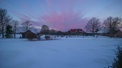 timelapse of a snowy landscape with two log cabins and a pink sky with clouds turning blue