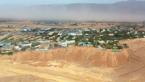 High-aerial-view-of-a-Negev-desert-sandstorm-behind-Kibbutz-Yotvata,-southern-Arava,-Israel-showing-modern-infrastructure