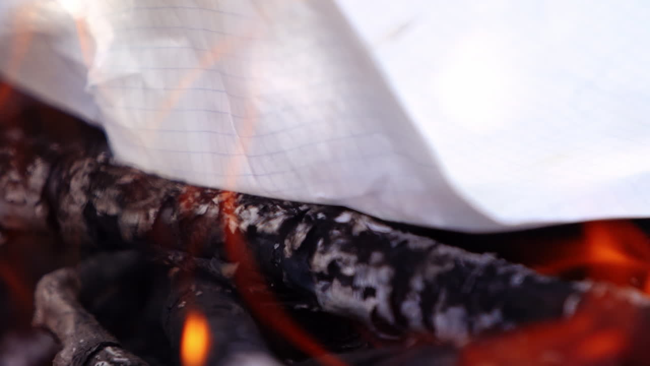 Paper and logs are burning in an outdoor fire. Flames all around. Campsite fire video.