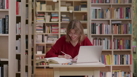 Glückliche-Junge-Frau,-Die-In-Der-Bibliothek-Lächelt-Und-Mit-Laptop-Studiert