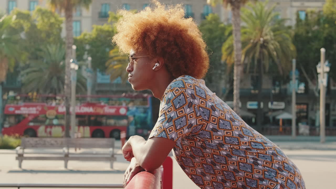 Young Man with Red Afro Hair and Earbuds Leaning on Railing