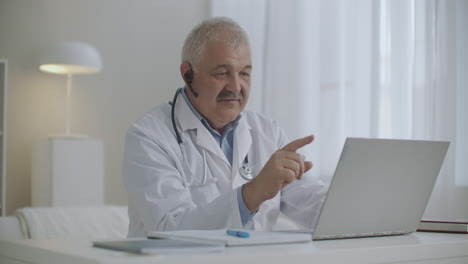 kind cheerful doctor is consulting online working by internet with patient chatting by video call from his laptop modern telemedicine