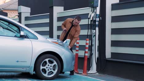 proceso de reabastecimiento de combustible de un automóvil eléctrico. un disparo debajo de la escotilla donde se carga el automóvil ecológico eléctrico. la escotella de carga del automóvil eléctrico se abre automáticamente. una mano masculina inserta un automóvil erecto