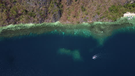 Cinematic-aerial-top-down-tilt-up-footage-of-the-shoreline-of-the-hilly-Palawan-with-a-boat-in-view-in-the-Philippines,-Asia,-Drone