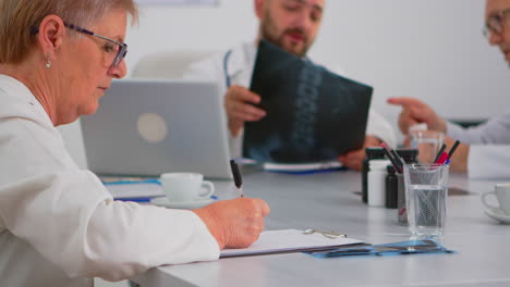 close up of senior woman doctor taking notes on clipboard