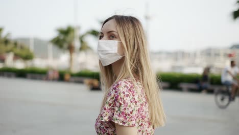 beautiful woman in dress and medical mask walking alone on city pier