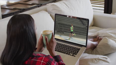 compuesto de una mujer sentada en casa sosteniendo café viendo un evento de salto de longitud de atletismo en una computadora portátil