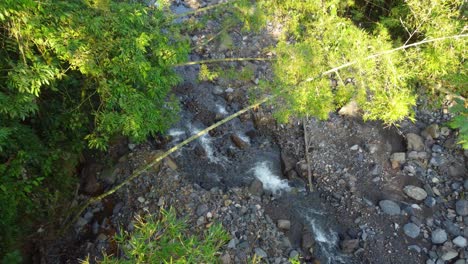 Disparo-De-Un-Dron-Descendiendo-Verticalmente-Hacia-Un-Pequeño-Arroyo-De-Agua-Dulce-Natural-Que-Fluye-Por-Una-Montaña-Rodeada-De-árboles-En-Risaralda,-Colombia