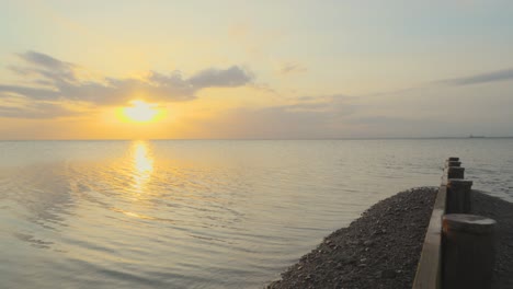 Slow-pan-across-calm-sea-horizon-showing-ships-and-breakwater-during-sunset-in-slow-motion-at-Fleetwood,-Lancashire,-UK