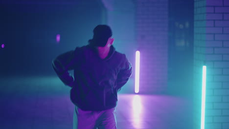 Ein-Mann-Aus-Stahl-Tanzt-Hip-Hop-Freestyle-Im-Modernen-Stil-In-Einer-Halle-Mit-Neonlicht-In-Violett-blauen-Farben.-Männlicher-Professioneller-Hip-Hop-Tänzer