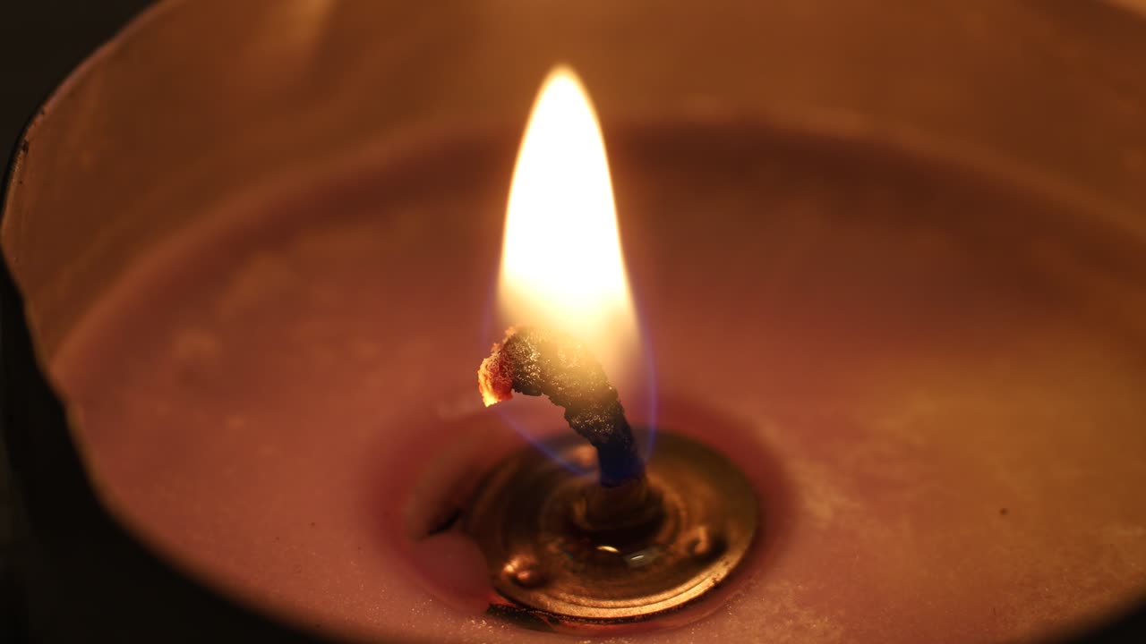 Primo piano di una fiamma di candela che brucia costantemente in una luce soffusa con una tenue luce arancione
