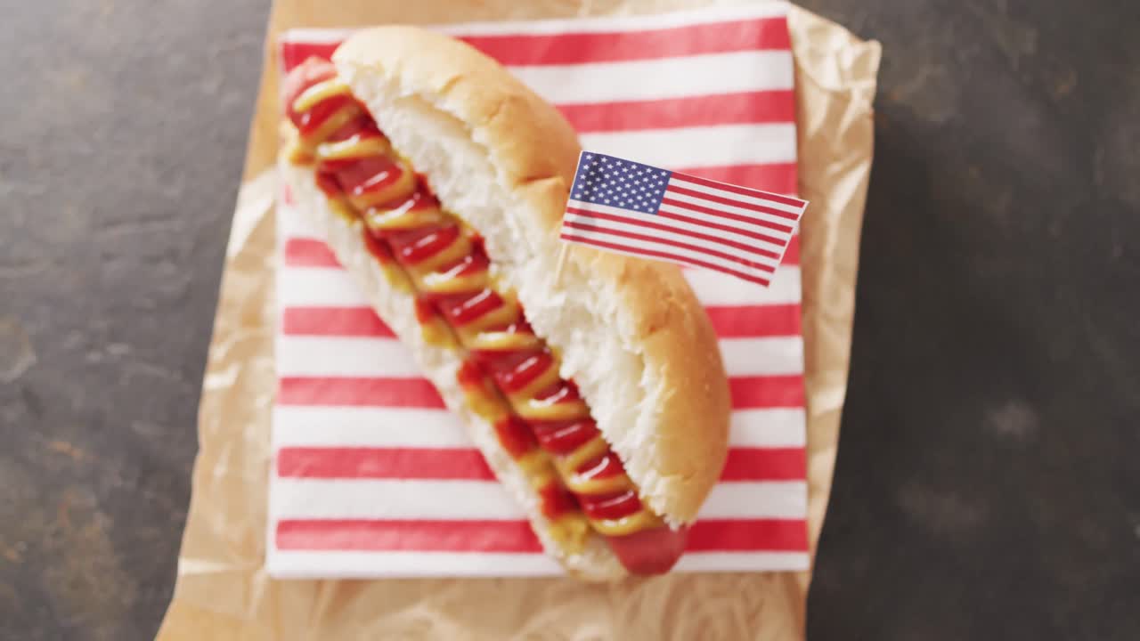 video de un perrito caliente con mostaza y ketchup con la bandera de ee.uu. en una superficie negra