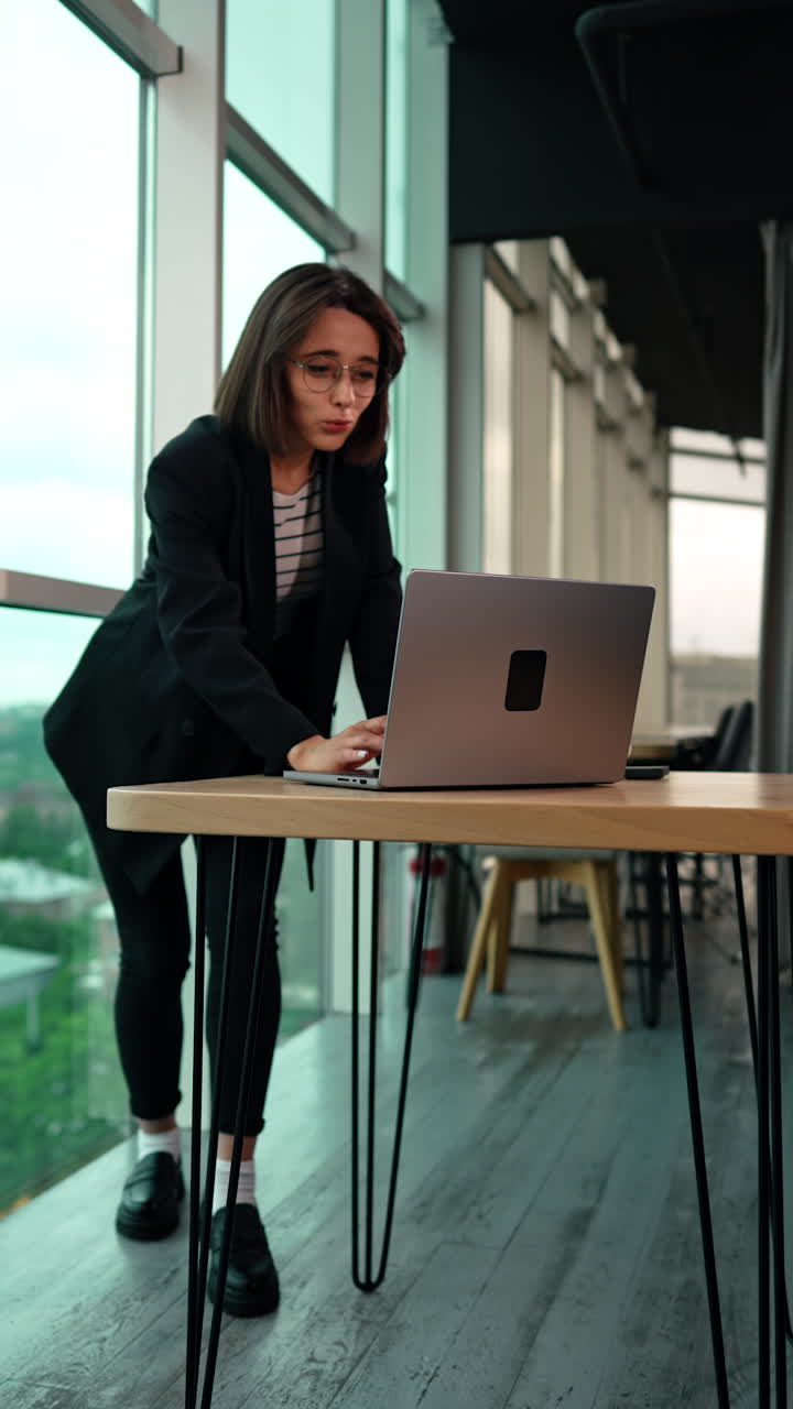 Happy rejoicing dark-haired woman in glasses. Lady working on her laptop gets good news or work results and feels good. Vertical video.