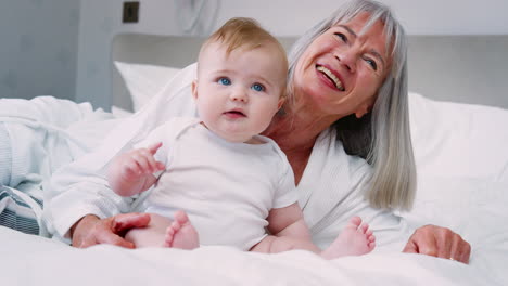 grandmother lying in bed at home looking after baby grandson