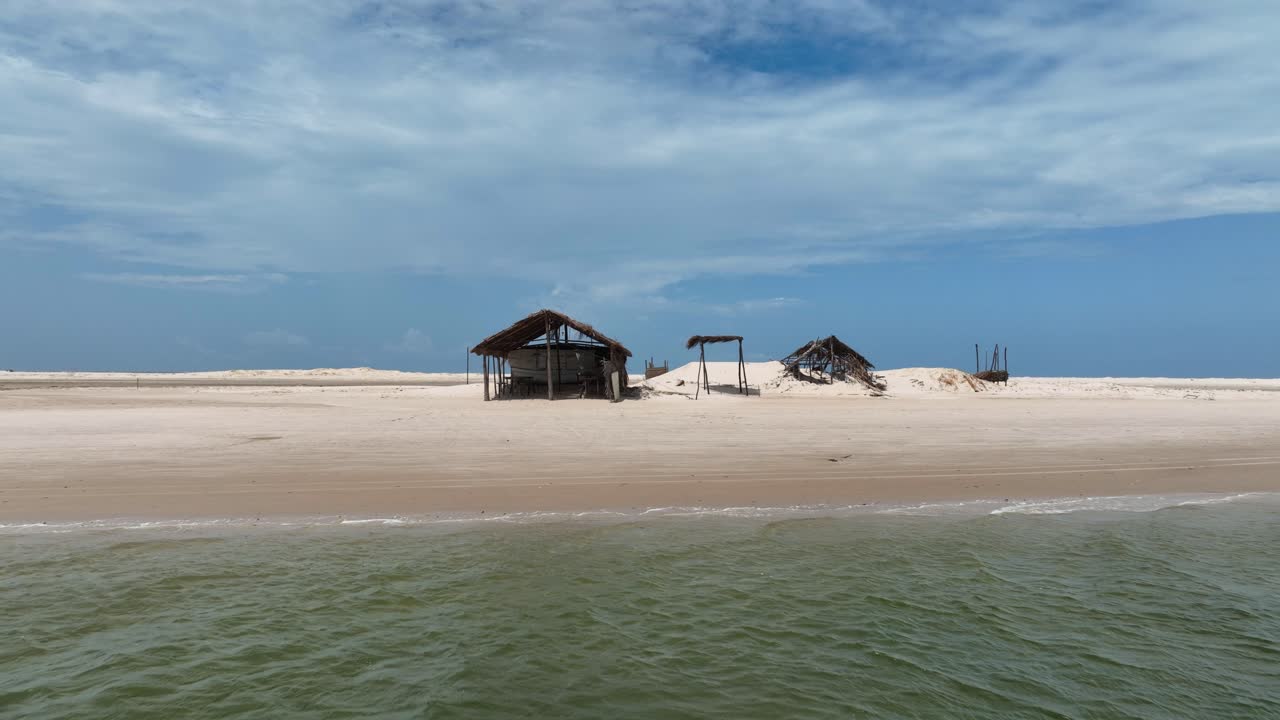 Straight backward aerial view over sandy huts on the beach, pulling back to reveal Parnaíba River waters, Brazil.