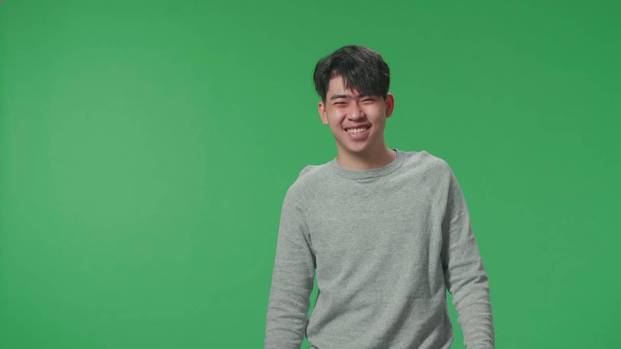 A Smiling Asian Man Dabbing While Standing In Front Of Green Screen Background