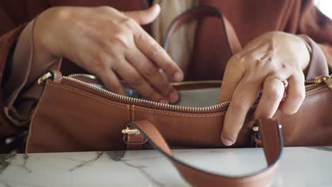 a woman's hand opening a brown leather bag