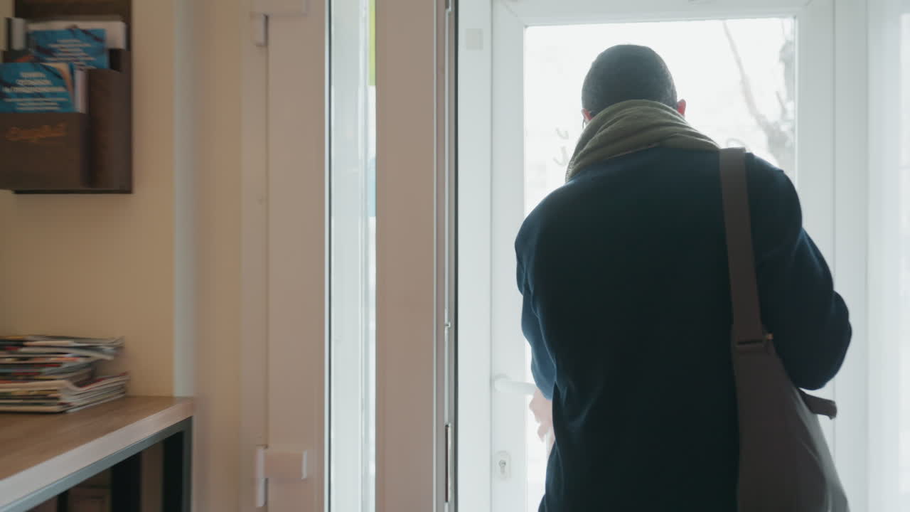 Man leaving cafe, back to camera, wearing scarf and shoulder bag commuter steps through doorway into bright street, quiet reflective mood, backlit silhouette and steady walk captured in sequence