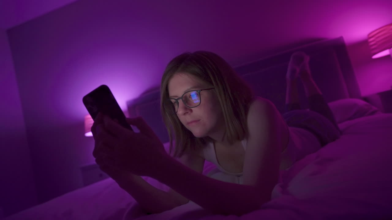 Girl browses social media on smart phone late at night in bedroom.