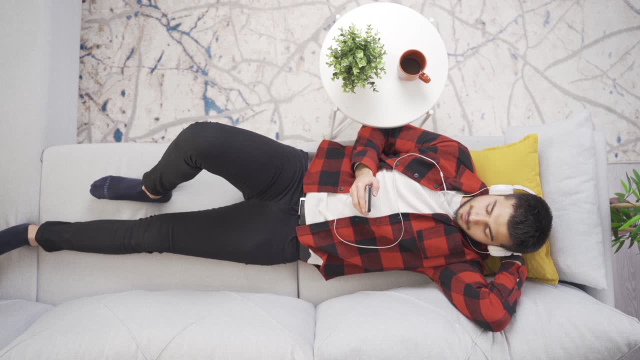 현대적인 집에서 소파에 혼자 누워 헤드폰으로 음악을 듣고 휴식을 취하는 남자.
