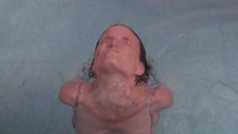 a young redhead woman swims towards the camera and smiles at the camera