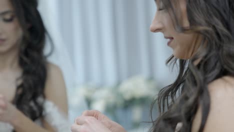 elegante novia morena haciendo pendientes en el espejo, hermoso cabello curry, novia bonita preparándose para la boda, mujer con sonrisa perfecta maquillaje rímel, novia joven y novia feliz en vestido blanco