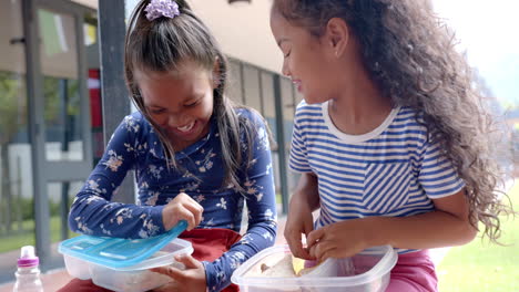 in school, two girls enjoying lunch from lunchboxes, smiling and chatting