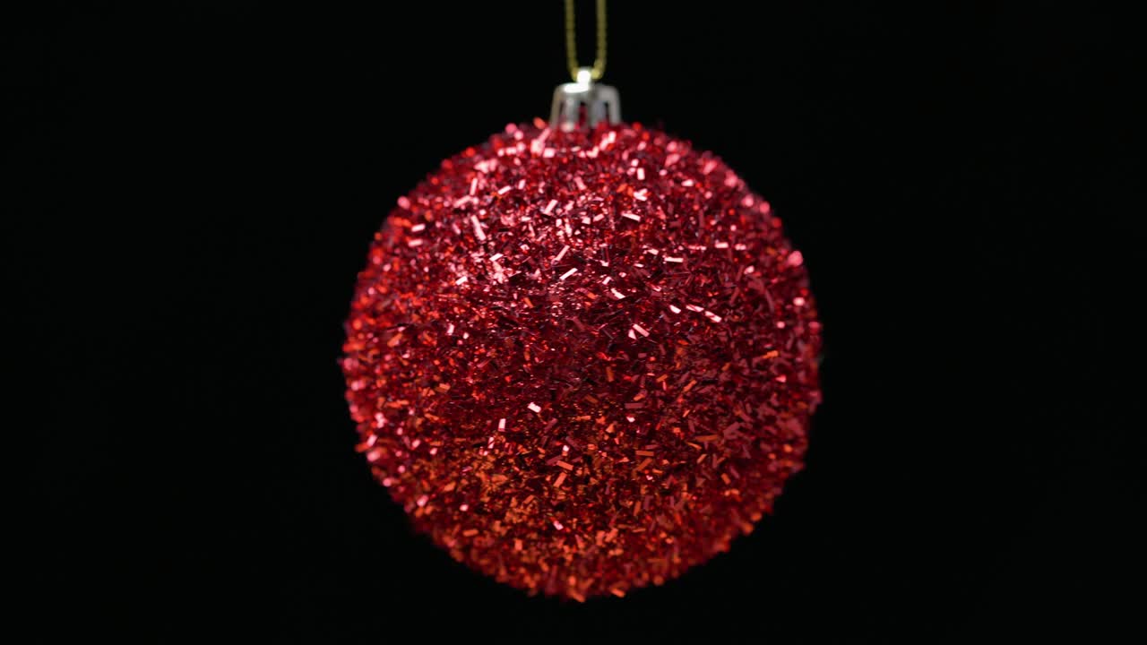 Close-up view of shiny bright red Christmas ball rotates on axis, hanging on black background. Celebration Xmas composition for Happy New Year